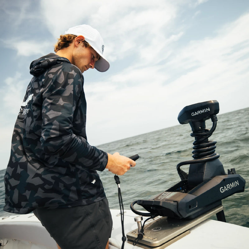 A man in a camo hoodie standing by the bow-mounted Garmin trolling motor, holding a small device