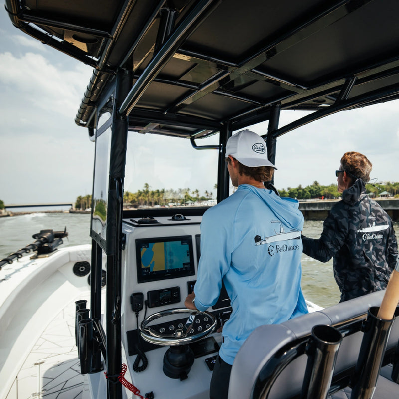 A captain in a white cap at the helm under the T-top, with a Garmin screen in front of him