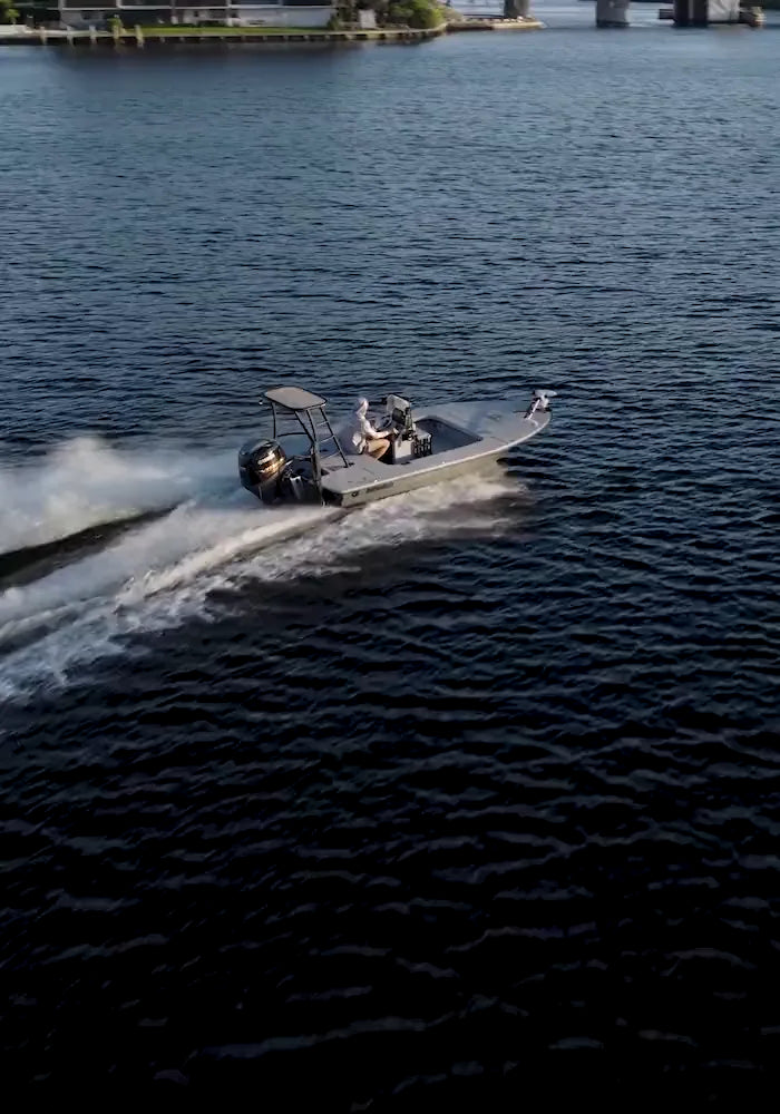 An aerial view of the small flats boat running across calm dark water, leaving a long white wake